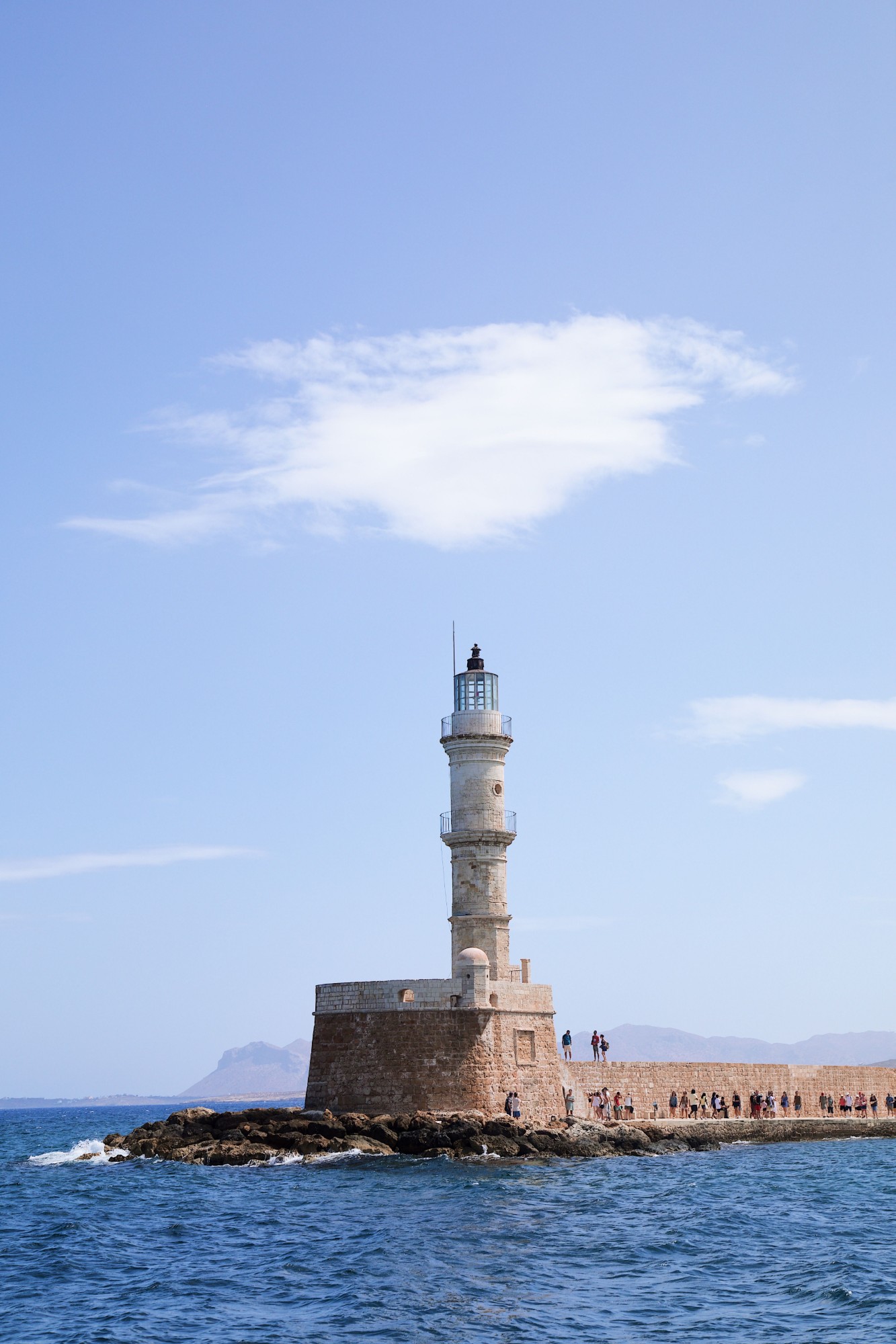 A stone lighthouse on a rocky pier under a blue sky